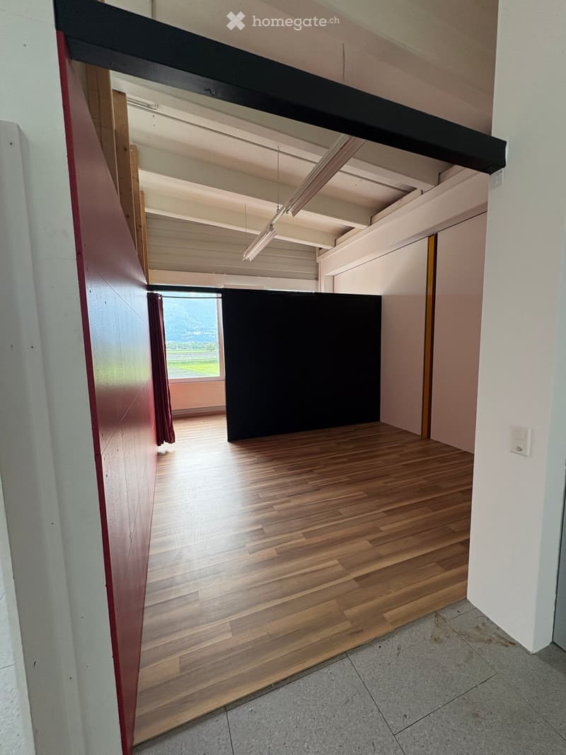 Empty room with wooden flooring, white walls, and a large window with a view of the outdoors. The room is unfurnished and has a modern, minimalist design.