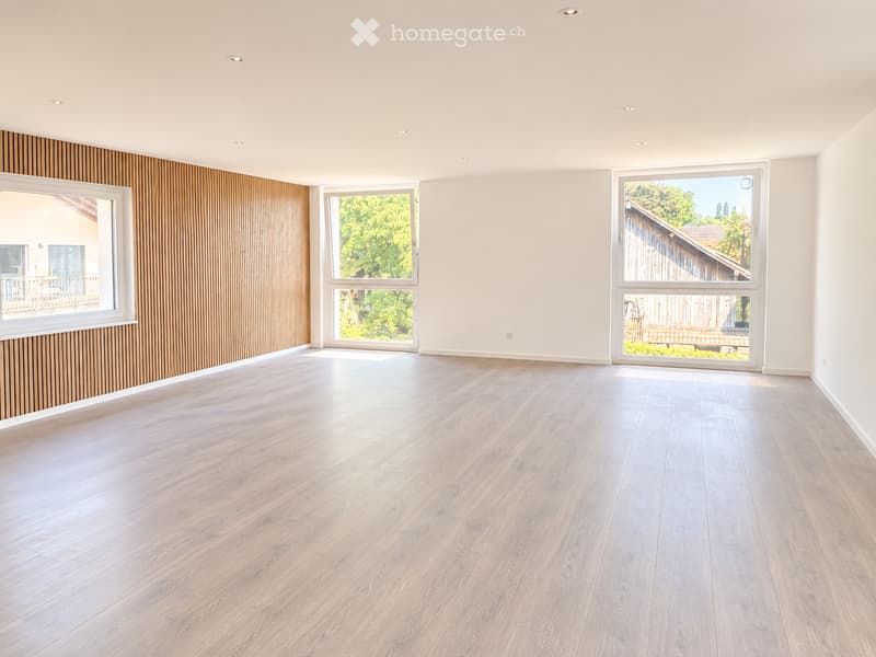 Empty room with light wooden flooring, white walls, large windows, and recessed ceiling lighting. No furniture or equipment present.