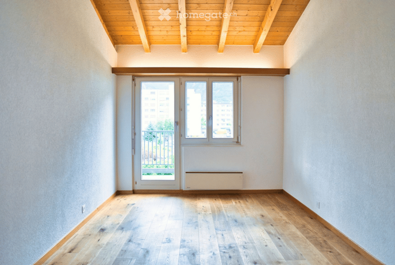 Empty room with wooden flooring, white walls, and a large window with a balcony view.