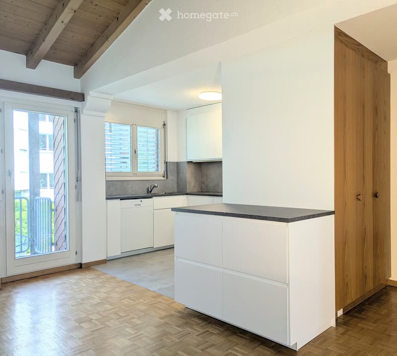 Modern kitchen with white cabinets, a central island, and a sleek countertop. Features include a dishwasher, a sink with a modern faucet, and large windows with blinds.