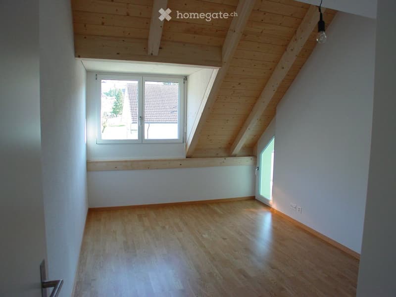 Empty attic room with wooden floor, white walls, skylight window, and exposed wooden ceiling beams.