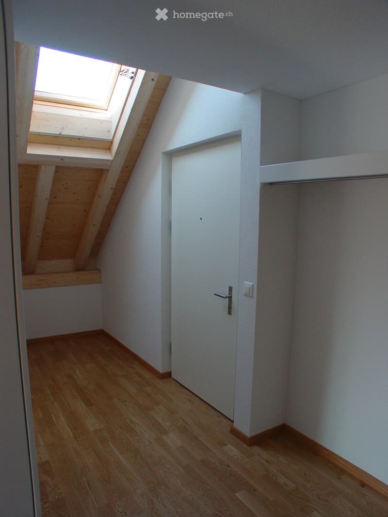 Empty room with wooden flooring, white walls, a white door, and a skylight window with wooden frame.