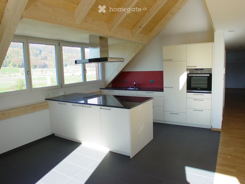 Modern kitchen with white cabinets, black countertops, and a central island. Features include a built-in oven, sink, and range hood, with large windows offering a view of the outdoors.