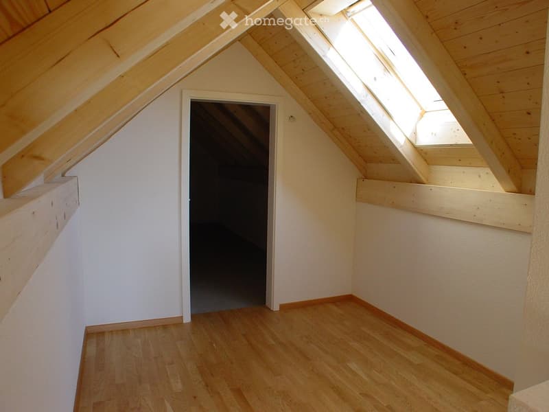 Empty attic space with wooden floors, white walls, exposed wooden beams, and skylights allowing natural light.