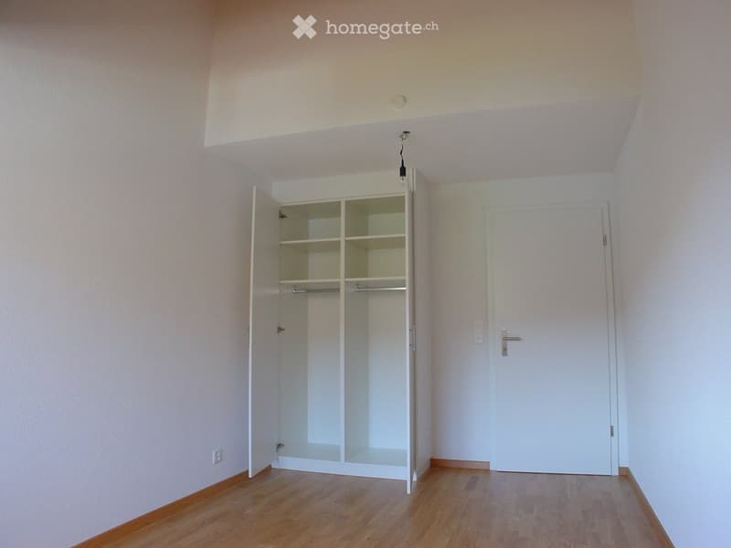 Empty room with wooden flooring, white walls, and an open closet with empty shelves. No furniture or personal items are present.
