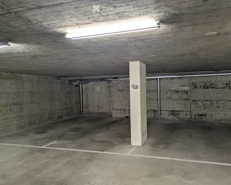 Empty underground parking space with concrete walls, a central pillar, and fluorescent lighting.