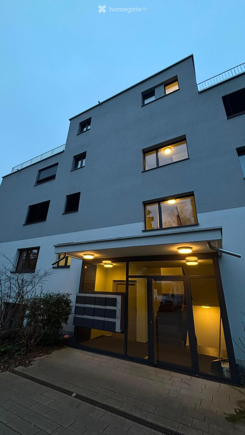 Modern two-story house with large windows, illuminated interior, and a raised ground floor entrance.