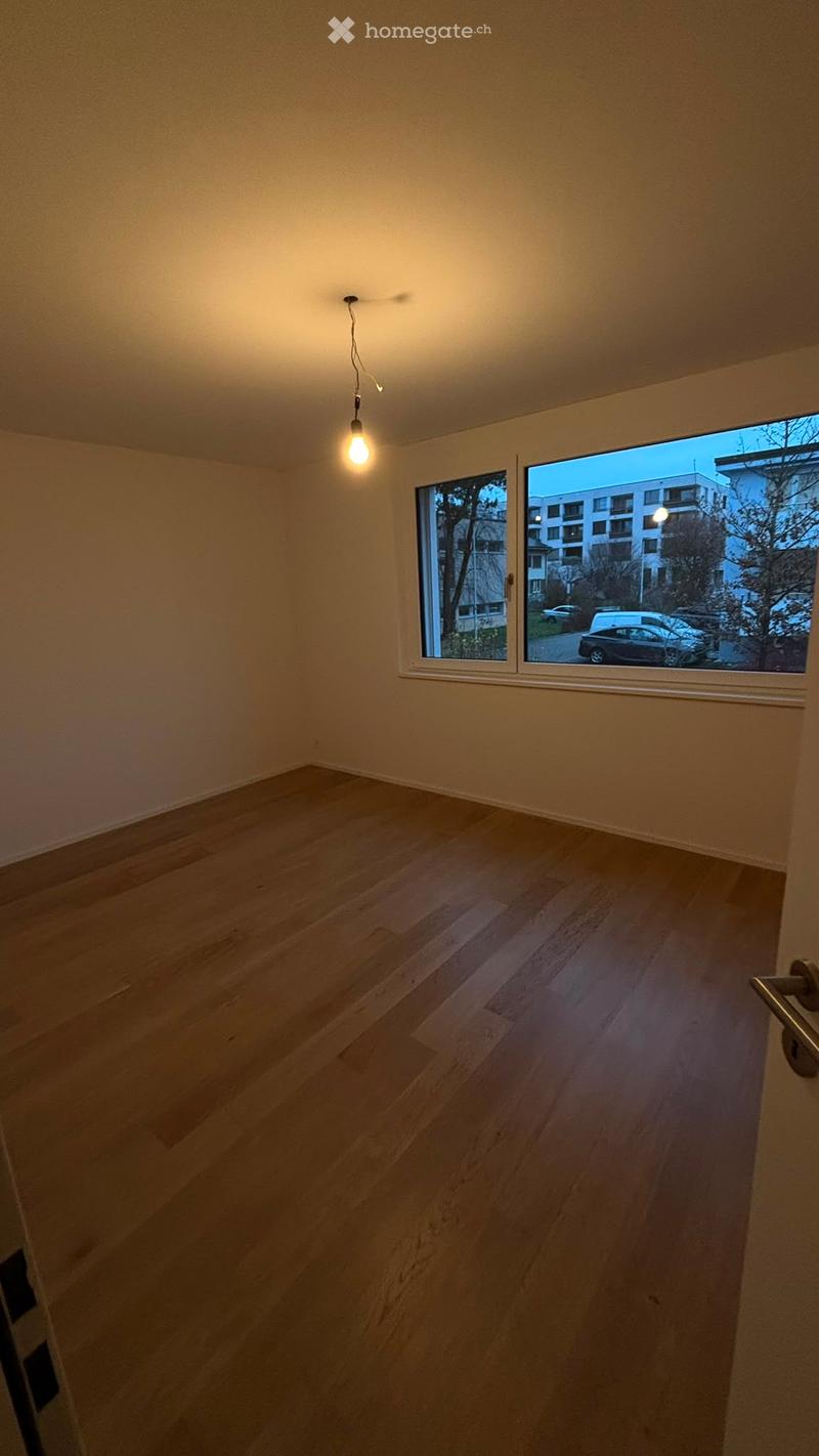 Empty room with wooden flooring, large windows, and a single hanging light fixture.