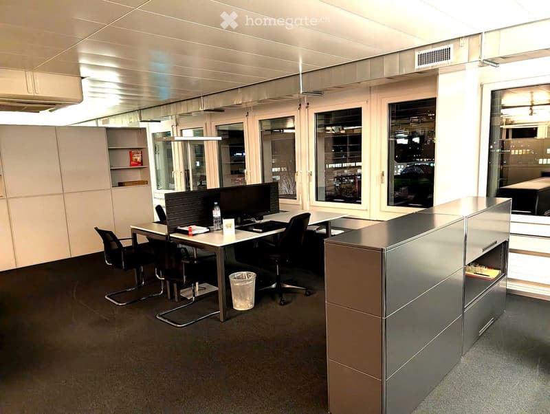 Modern office space with desks, chairs, computers, and large windows overlooking the city.