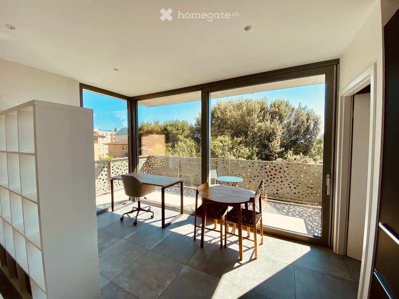 Modern balcony area with tiled floor, large glass doors, and outdoor furniture including a table and chairs.