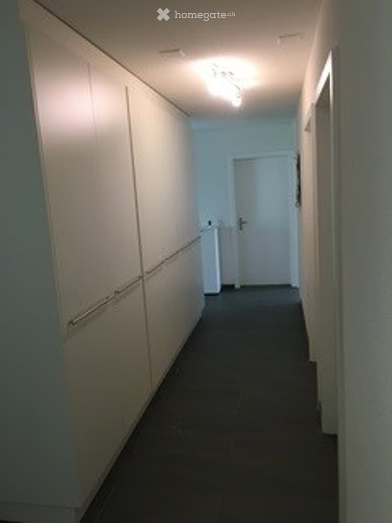 Empty hallway with white walls, dark carpeted floor, and a closed white door at the end.