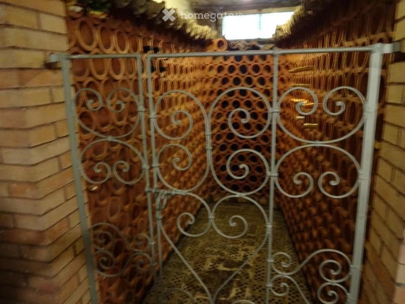 A narrow hallway with a metal gate, brick walls, and a patterned floor. The gate features ornate scrollwork and is set between two brick walls.