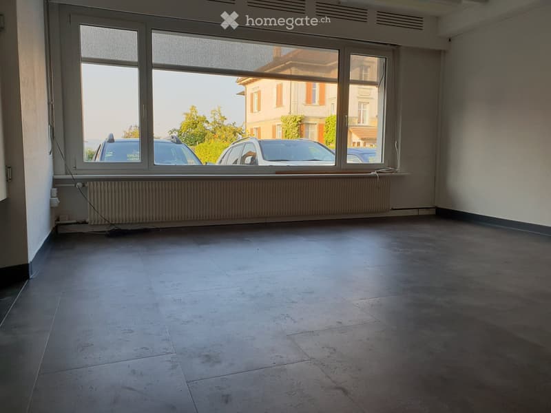 Empty room with large windows, tiled floor, radiator, and visible cars outside.
