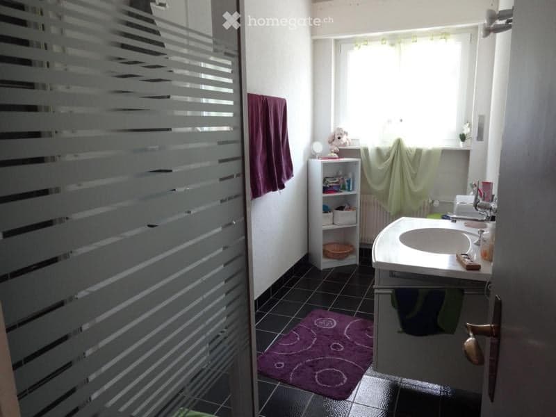 Bathroom with a white sink, faucet, radiator, small shelf, purple towel, and a purple rug on the floor.