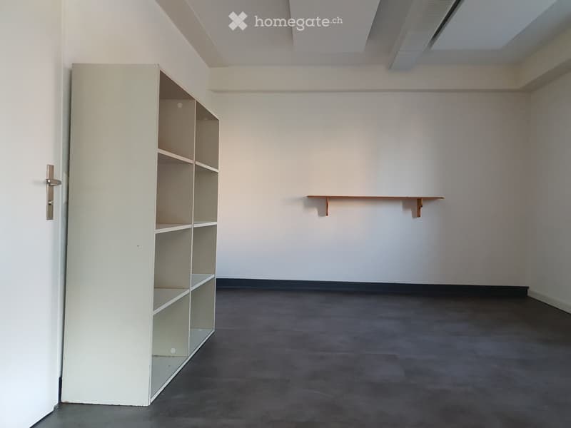 Empty room with a grey carpeted floor, white walls, a white shelving unit, and a small wooden shelf on the wall.
