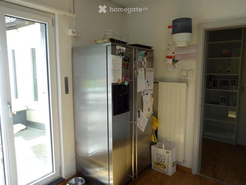 Modern kitchen with stainless steel refrigerator, radiator, shopping bag, and pet bowl on the floor.