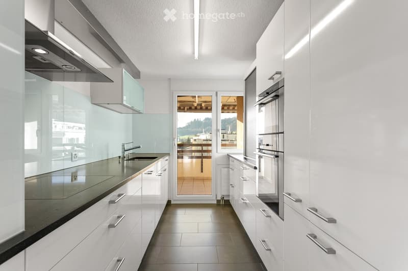 Modern kitchen with white cabinets, stainless steel appliances, and a sleek black countertop. Features a built-in oven and a sink with a modern faucet.