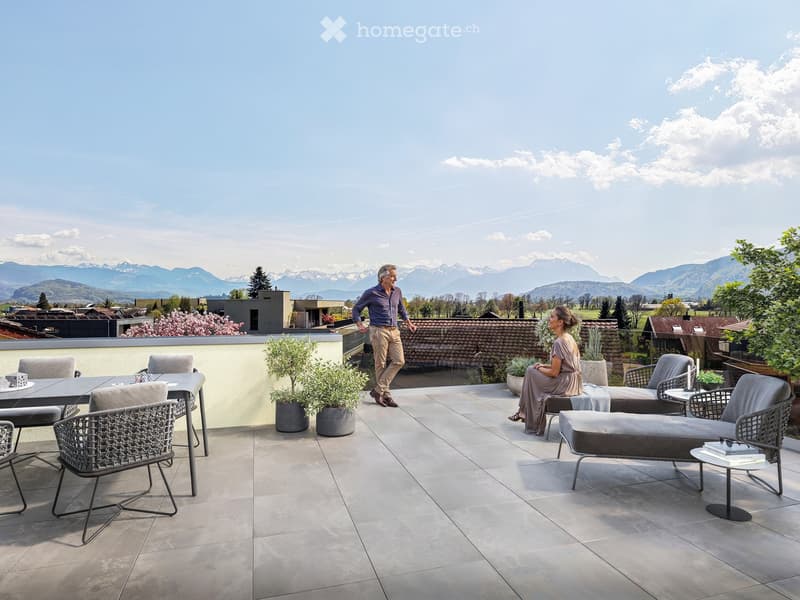 A spacious balcony with modern furniture, including a table, chairs, a sofa, and potted plants, overlooking a scenic mountain view.