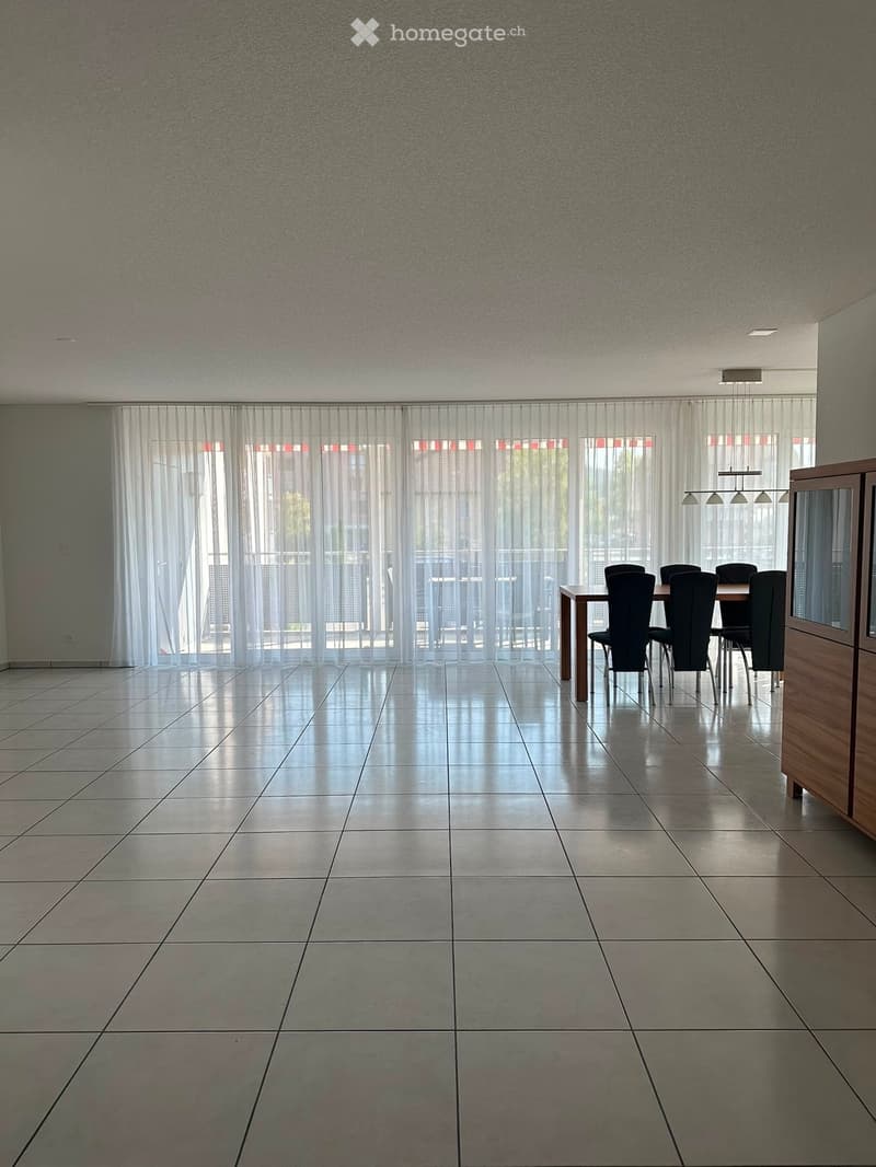Dining room with tiled floor, large windows with sheer curtains, and a dining table with chairs.
