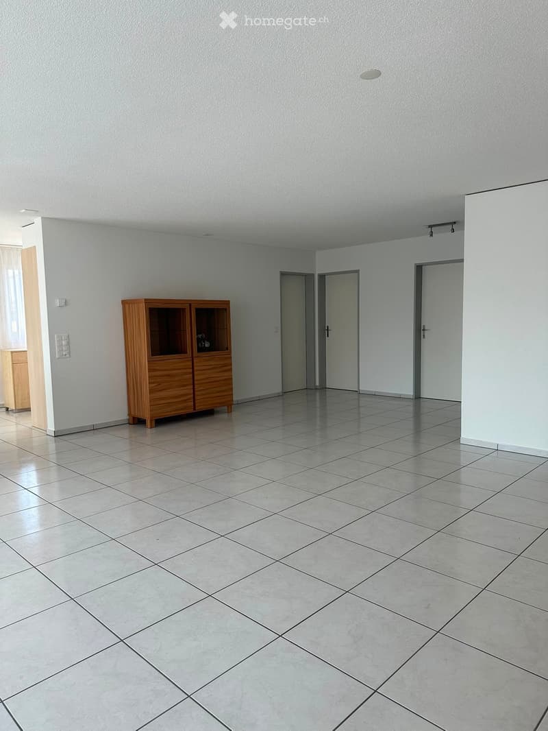 Empty room with tiled floor, white walls, and a wooden cabinet with glass doors.