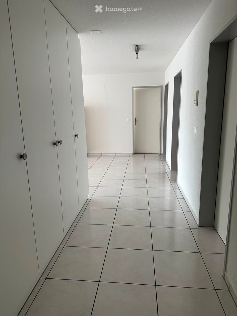 Empty hallway with tiled floor, white walls, and several doors leading to other rooms.