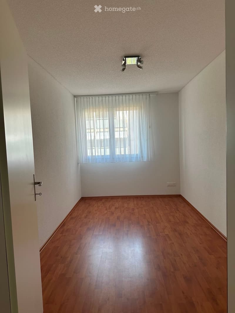 Empty room with wooden flooring, white walls, and a window with sheer curtains. No furniture or equipment is present.