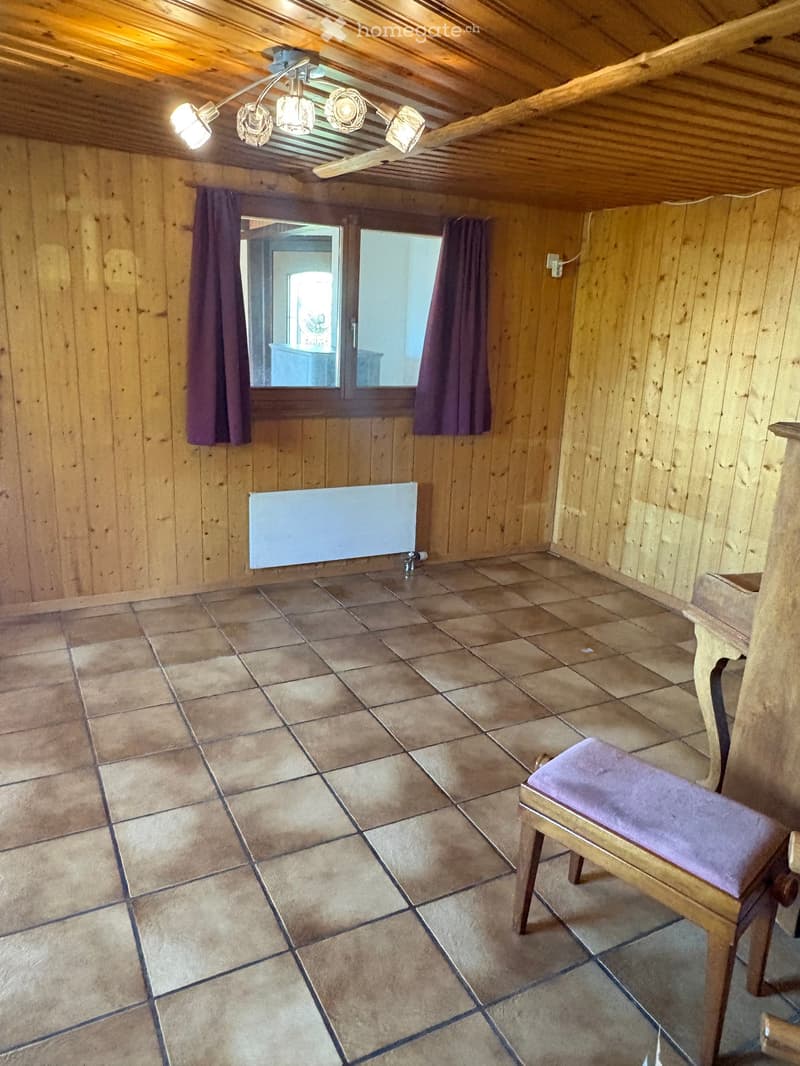 Wooden-paneled room with tiled floor, a single chair with a purple cushion, a radiator, and a window with curtains.