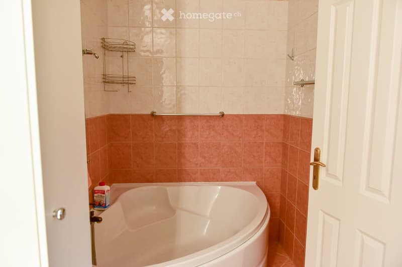 white bathtub, tiled walls, cleaning product on the side