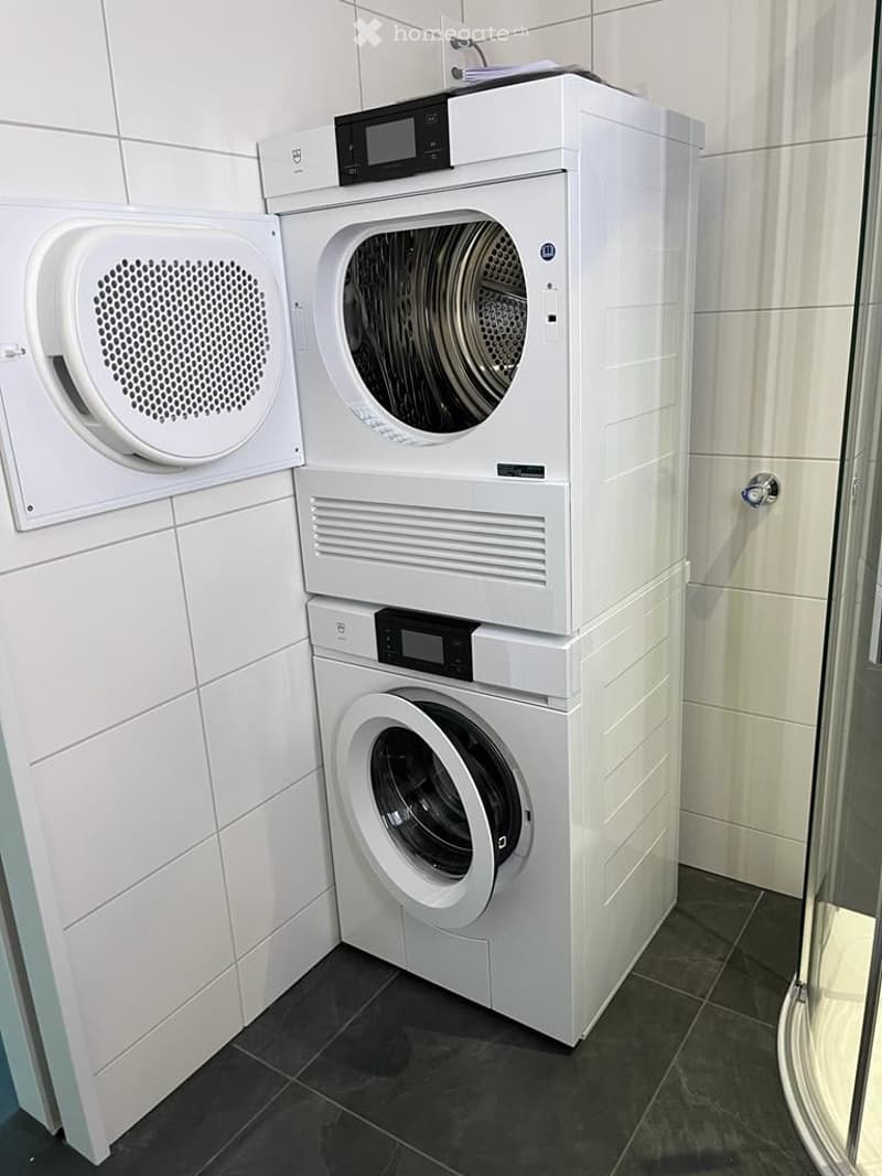 Modern bathroom with a private washing machine and dryer unit, white tiled walls, and dark tiled floor.