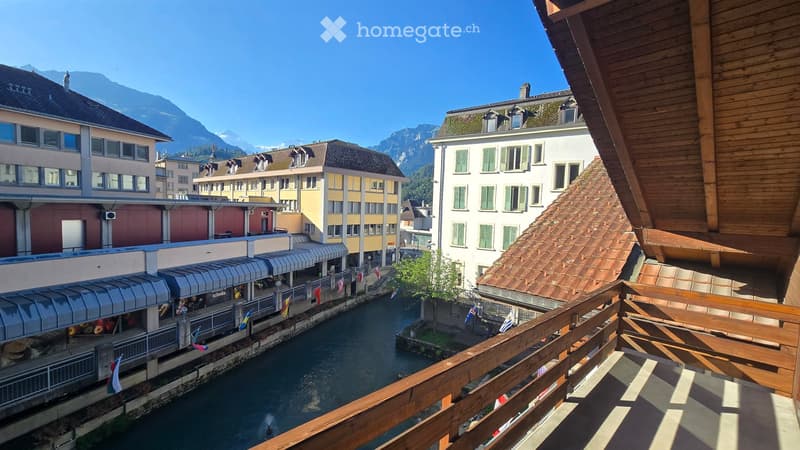 Balcony overlooking a canal with surrounding buildings and mountains in the background.