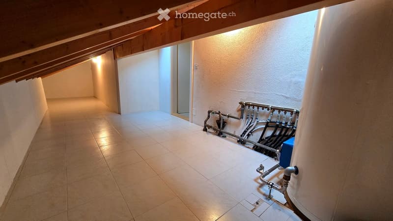 Clean, well-lit hallway with tiled flooring and exposed wooden beams on the ceiling. Plumbing pipes and a water heater are visible on one wall.