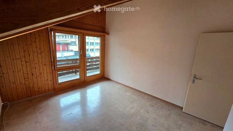 Empty room with tiled floor, wooden paneled wall, large window with wooden frame, and a door.