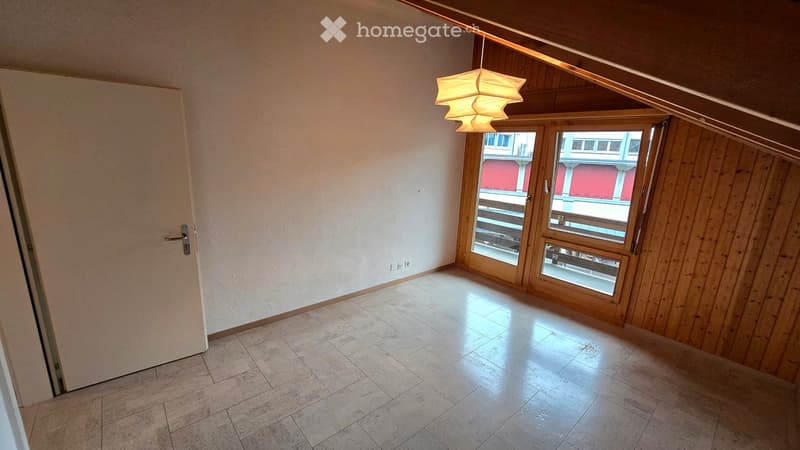 Empty room with tiled floor, wooden walls, large window with view, and hanging light fixture.