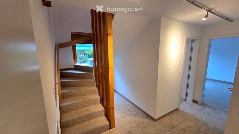 Hallway with tiled floor, carpeted staircase, and a view of a balcony or outdoor area through a glass door.
