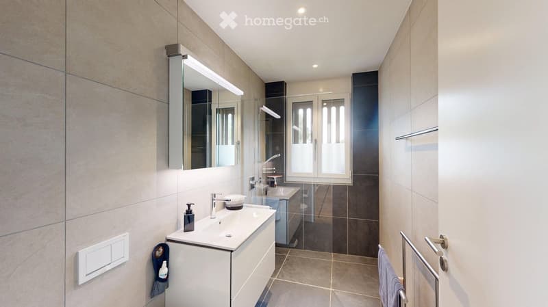 Modern bathroom with a white sink, chrome faucet, large mirror with built-in lighting, and a glass-enclosed shower area.