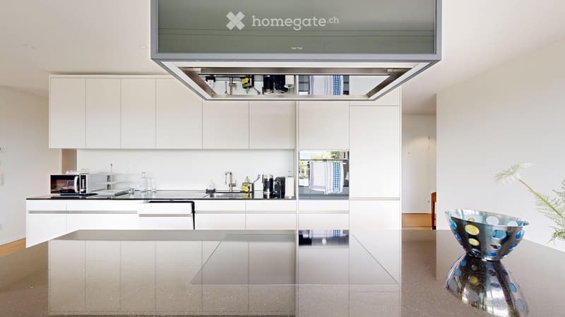 Modern kitchen with white cabinets, stainless steel appliances, and a sleek island. Features a microwave, sink, and decorative bowl on the counter.