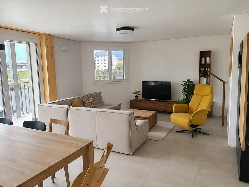 Modern living room with a grey sectional sofa, yellow armchair, wooden coffee table, dining table with chairs, TV, bookshelf, and plants.