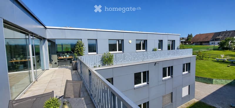 Modern balcony with glass railing, outdoor furniture, and view of a green lawn and countryside.