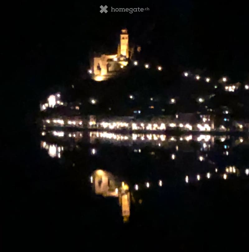 Nighttime view of a coastal town with illuminated buildings and lights reflecting on the water.
