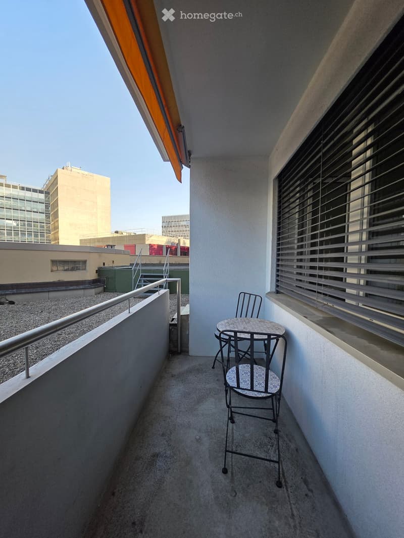 Balcony with a small round table and two chairs, metal railing, and an orange awning.