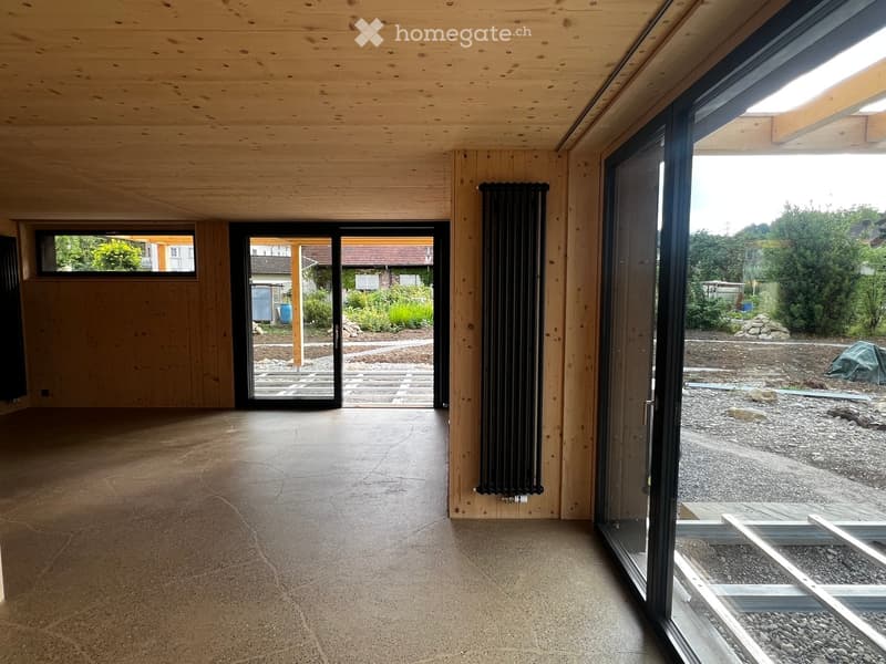 Empty room with wooden walls and ceiling, concrete floor, large sliding glass doors leading to outdoor area, radiator on wall.