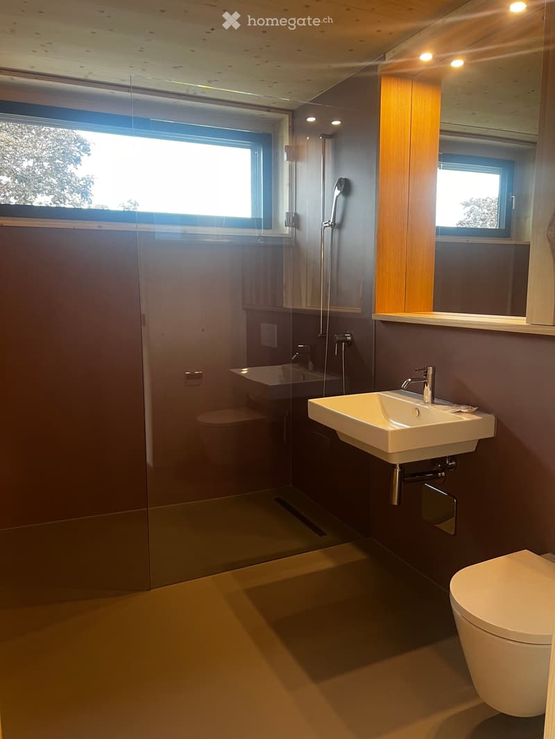 Modern bathroom with a white sink, chrome faucet, toilet, bathtub, and a glass-enclosed shower area. Features a large window and a mirror above the sink.
