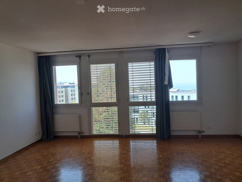 Empty room with wooden flooring, large windows with blinds, and radiators. No furniture or personal items present.