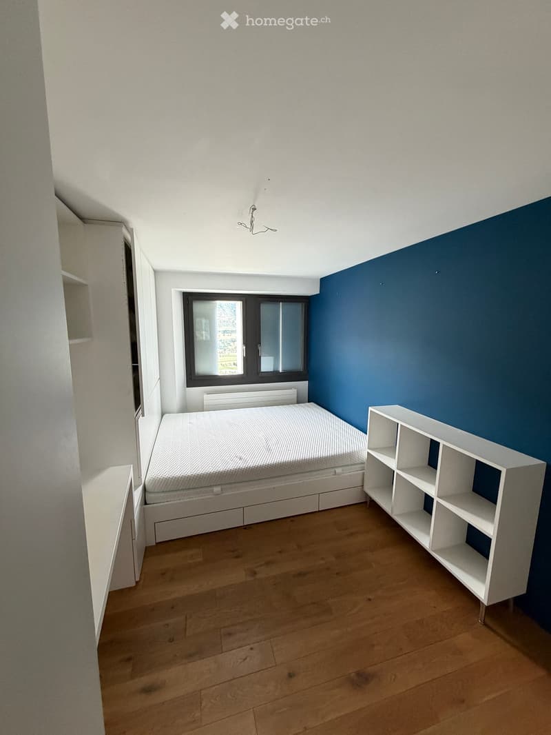 Minimalist bedroom with a bed, a white shelf, and wooden flooring.
