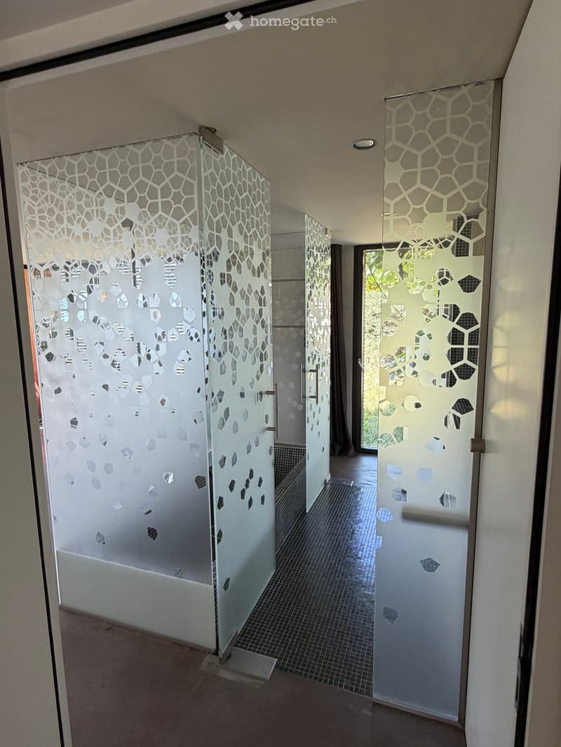 Modern hallway with glass partitions featuring geometric patterns, tiled floor, and recessed lighting.