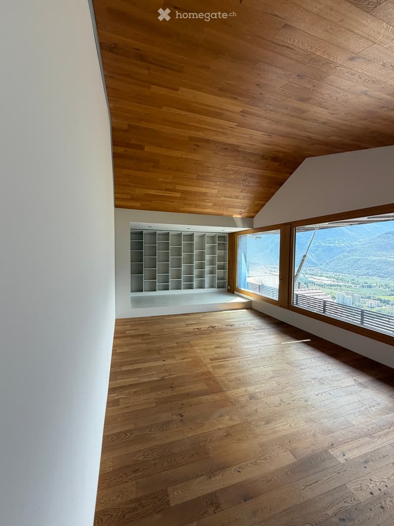 Empty room with wooden flooring and white walls, featuring built-in shelving and large windows with scenic mountain views.