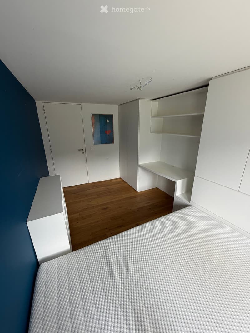 Modern bedroom with a white bed, built-in white wardrobe with shelves, and a small picture frame on the wall.