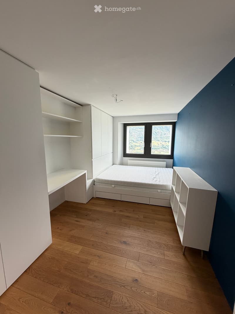 Modern, minimalist bedroom with a single bed, built-in white shelves, and a large window offering a scenic view.