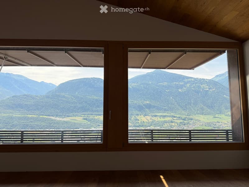 Empty room with large windows offering a scenic mountain view, wooden floor, and simple wooden window frames.