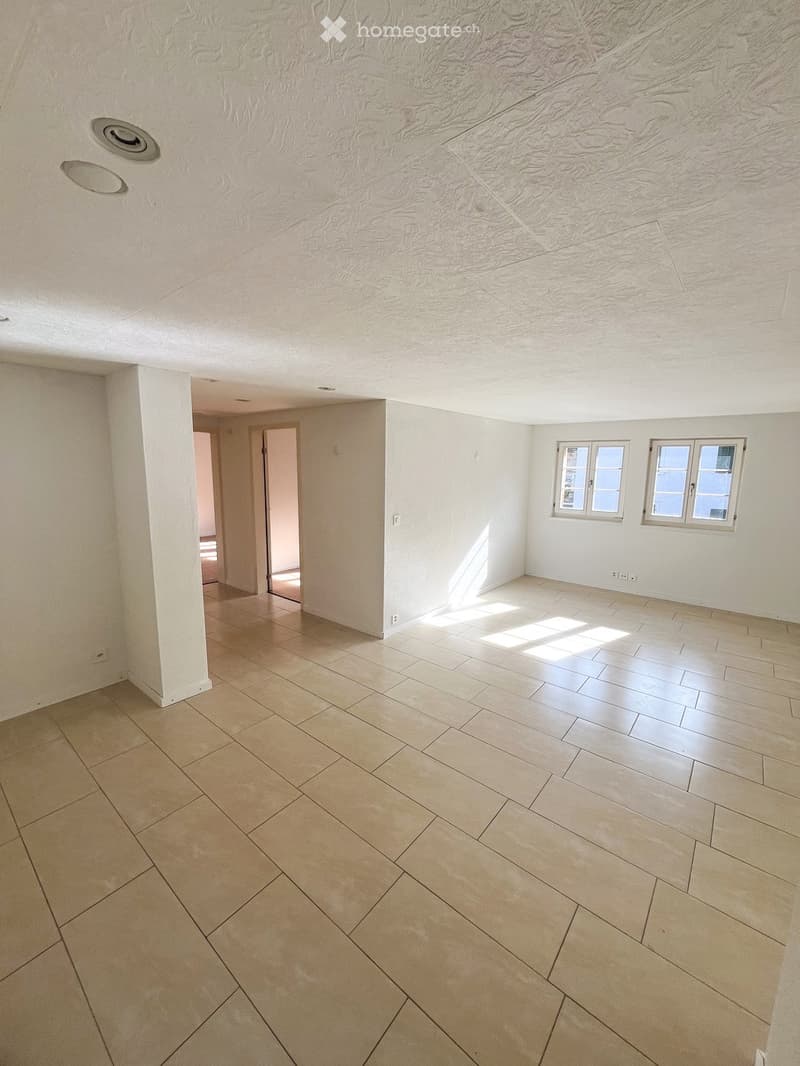 Empty room with light-colored tiled flooring, white walls, and two windows allowing natural light. The ceiling features recessed lighting and a textured finish.